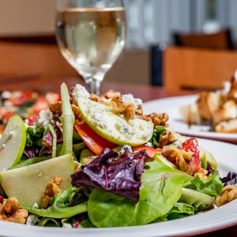 A fresh salad with mixed greens, sliced apples, walnuts, and blue cheese crumbles, with white wine.