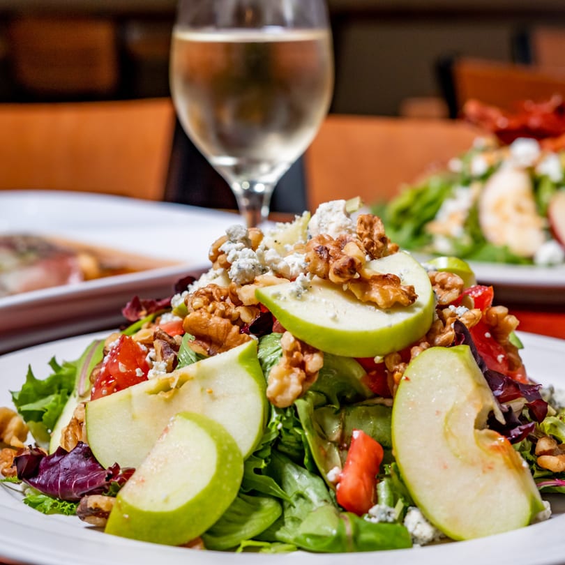 Lido's Restaurant & Pizzeria's apple and walnut salad with blue cheese and tomatoes, with a glass of white wine.