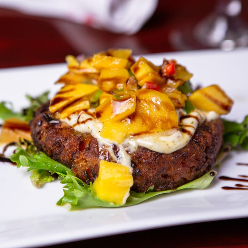 A dark brown patty topped with mango salsa, creamy sauce, and balsamic glaze on lettuce.