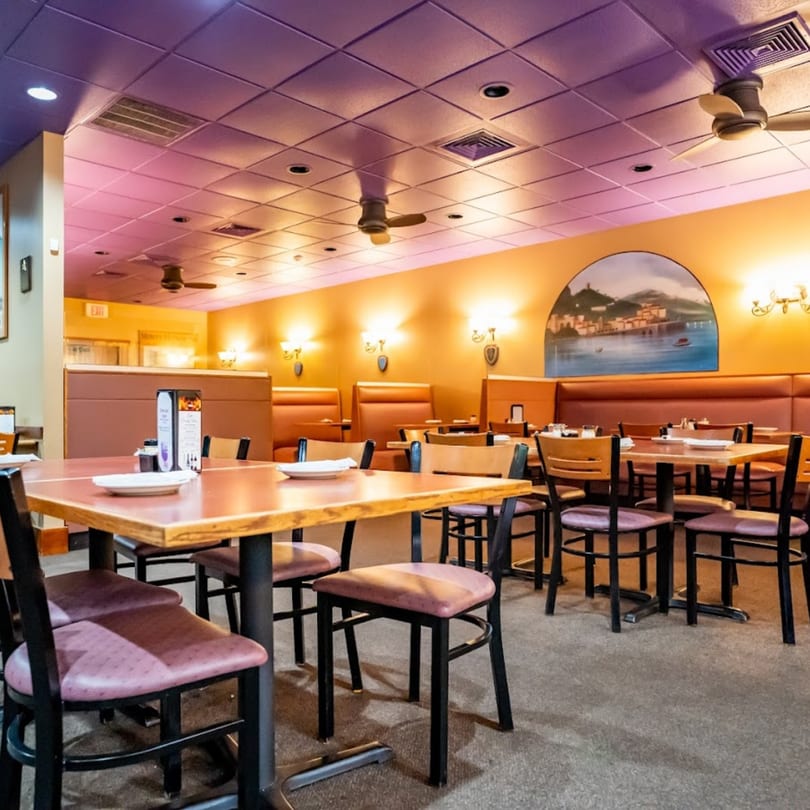 Interior of Lido's Restaurant & Pizzeria, showing dining tables, booths, and a mural of an Italian village.