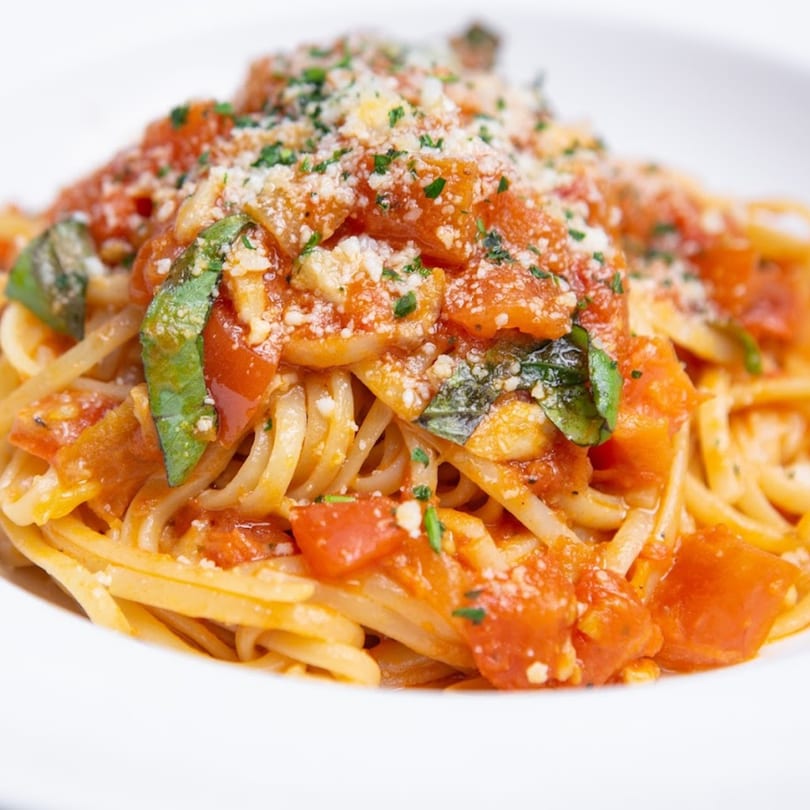Close-up of Lido's linguine pasta with chunky tomato sauce, fresh basil, and grated cheese.