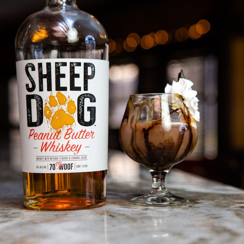 A bottle of Sheep Dog Peanut Butter Whiskey next to a cocktail with whipped cream and chocolate drizzle.