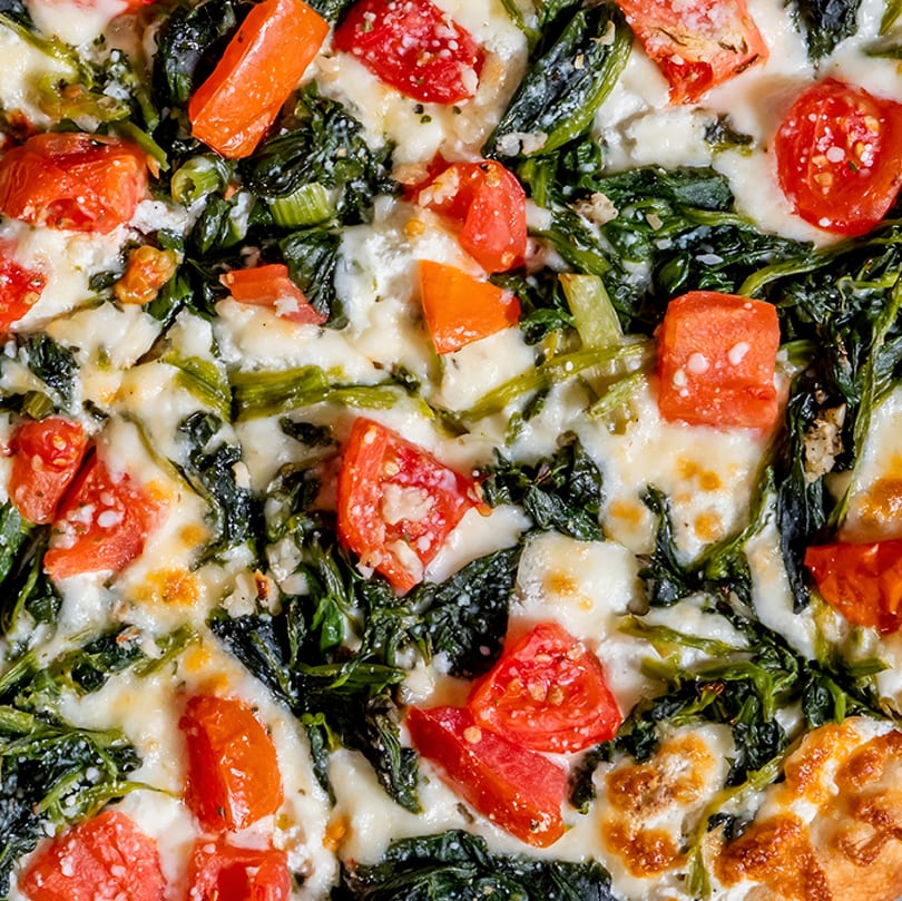 Close-up of a Lido's pizza with melted cheese, spinach, and diced tomatoes.