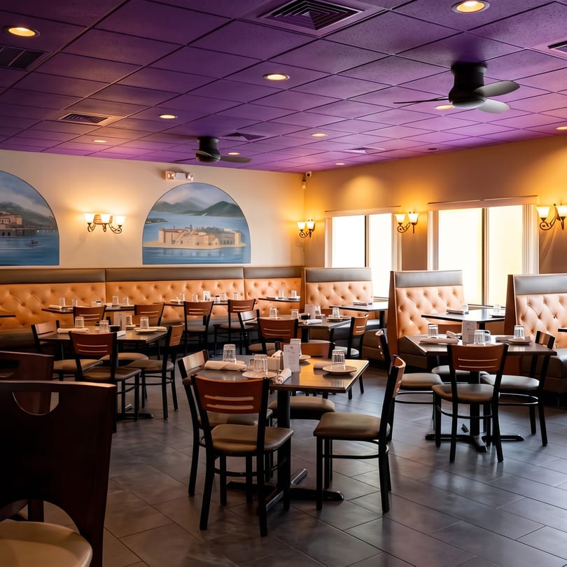 Empty restaurant dining room with set tables, booths, and murals of coastal towns on the walls.