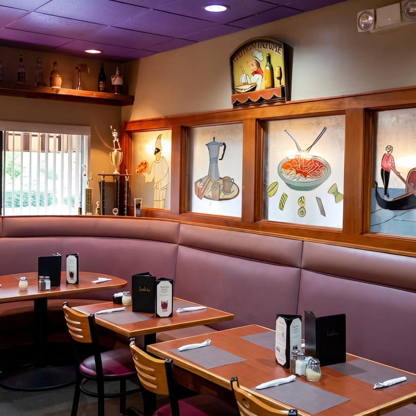 An Italian restaurant interior with purple ceiling, booth seating, and framed art depicting Italian scenes.