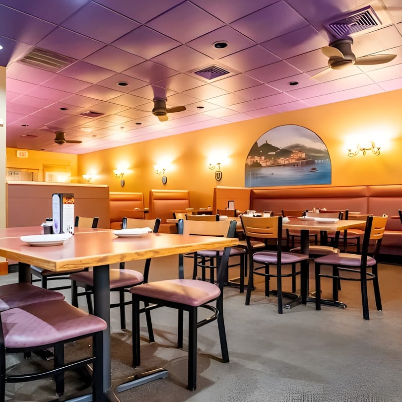 Empty restaurant dining room with purple ceiling, orange walls, booth seating, and tables set for service.